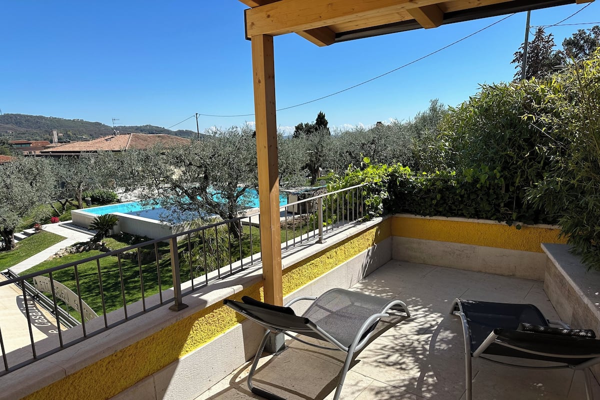 A balcony with a pool view, outdoor seating, and a yellow wall.
