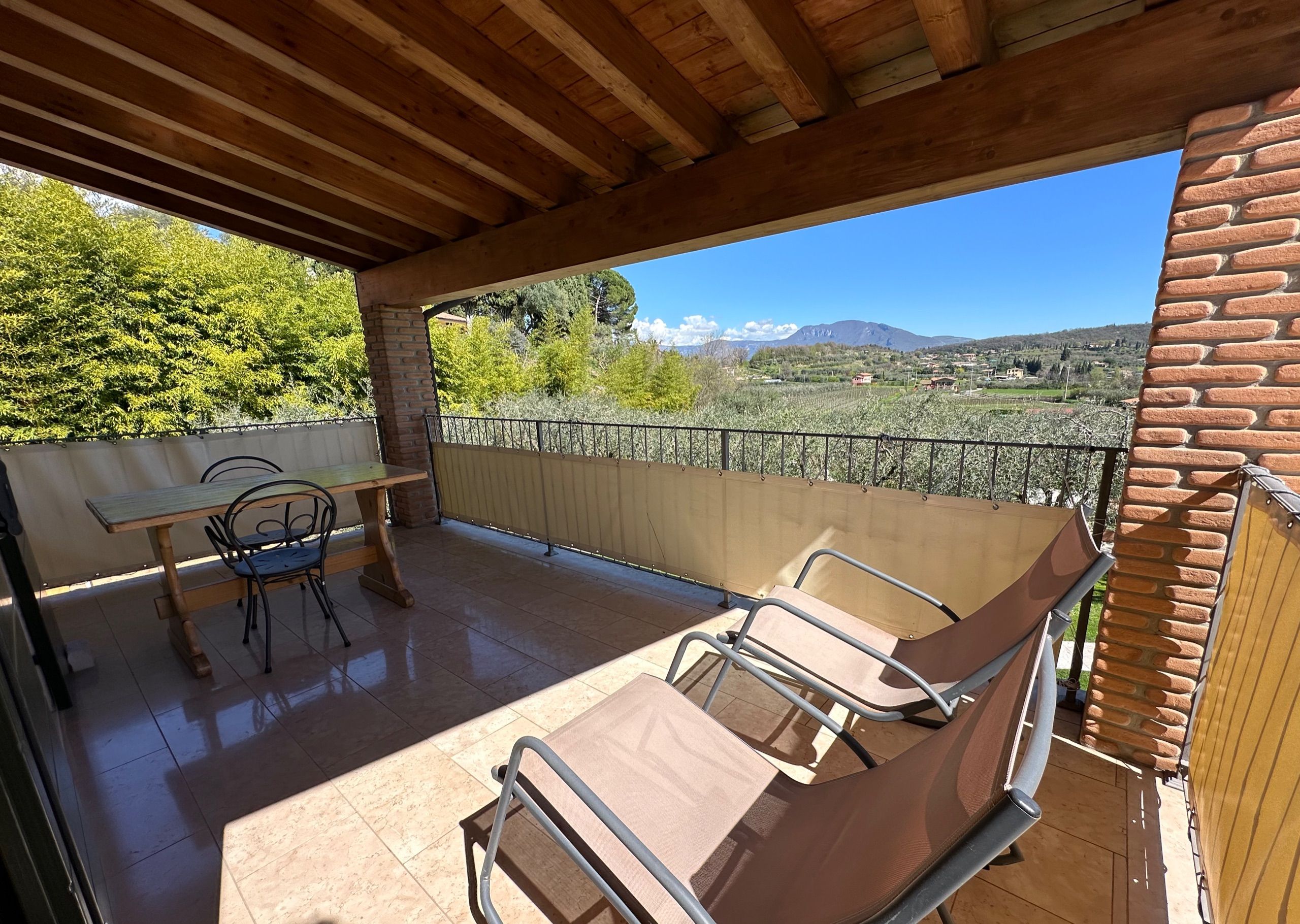 Un patio techado con mesa y sillas, vista al campo y un muro de ladrillo.