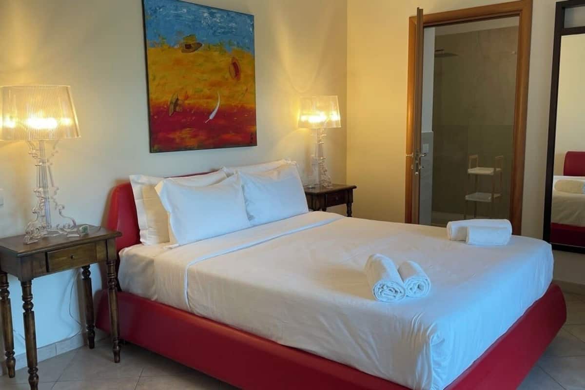 A hotel room with a bed, two bedside tables, a painting on the wall, a mirror, and a door.