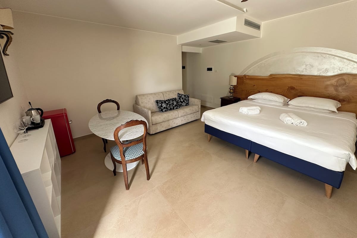A hotel room with a bed, a sofa, a dining table, and a chair.