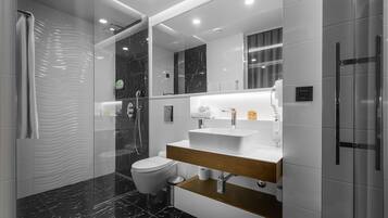 Un baño moderno con cabina de ducha de vidrio, inodoro blanco, tocador con encimera de mármol y un espejo grande.