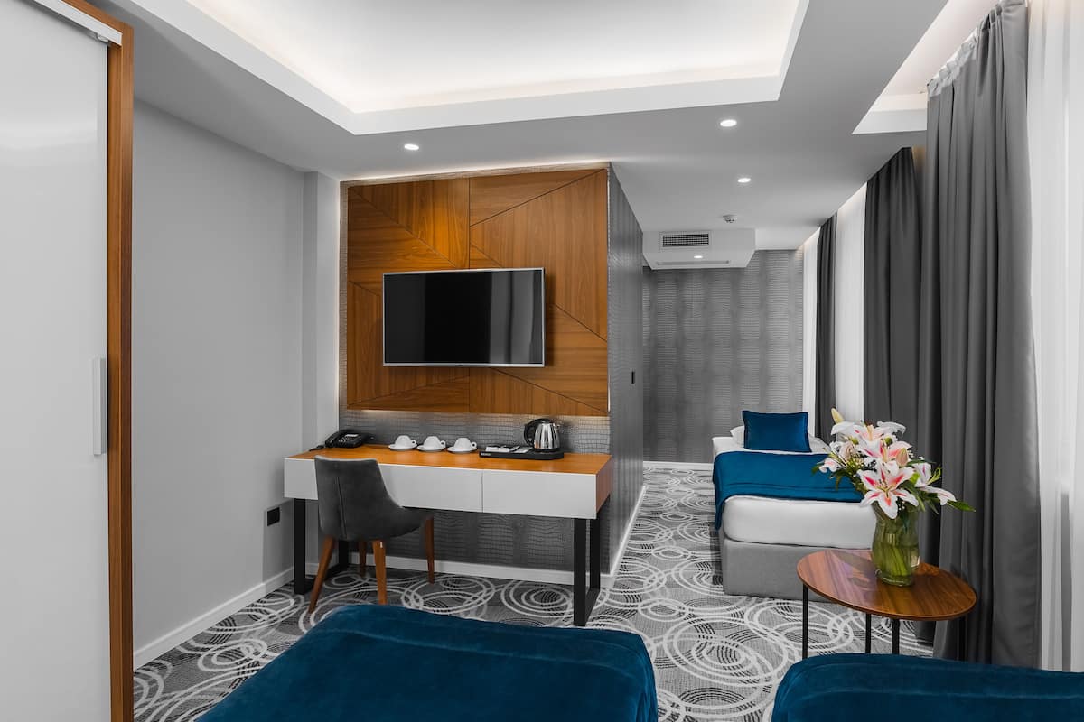 A modern hotel room with a desk, a flat-screen TV, a sofa, a small table, and a vase of flowers.