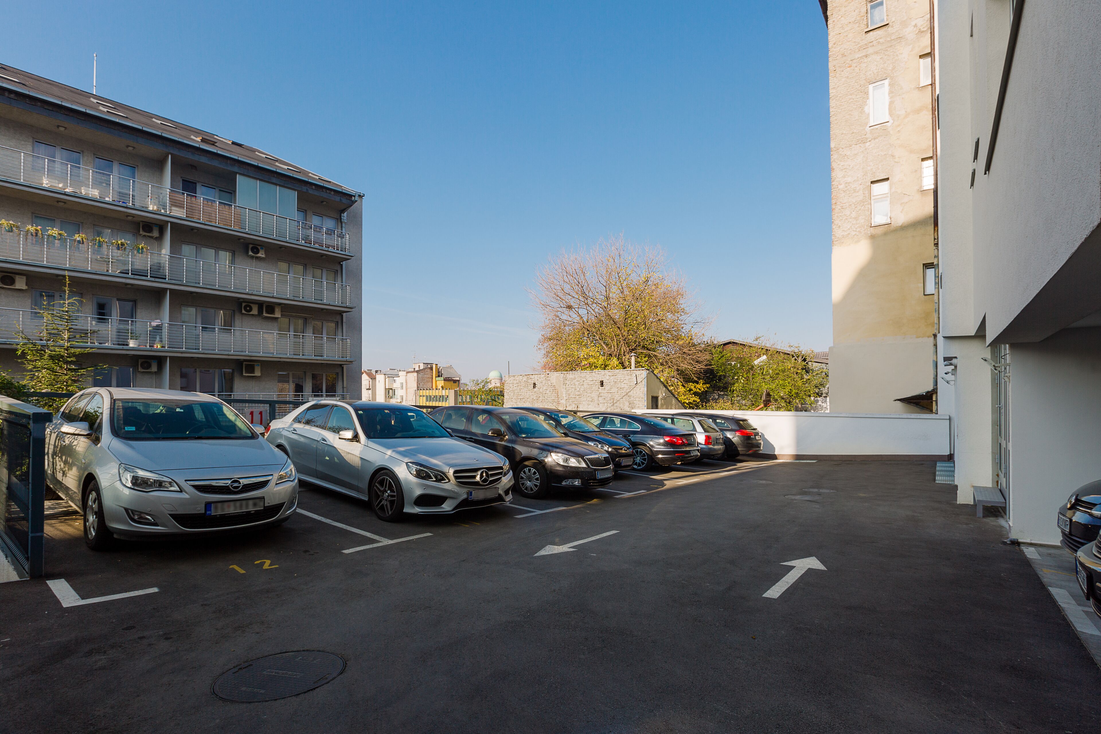 Ein Parkplatz mit mehreren in Reihe geparkten Autos neben einem Mehrstöckiger Gebäude mit Balkonen.