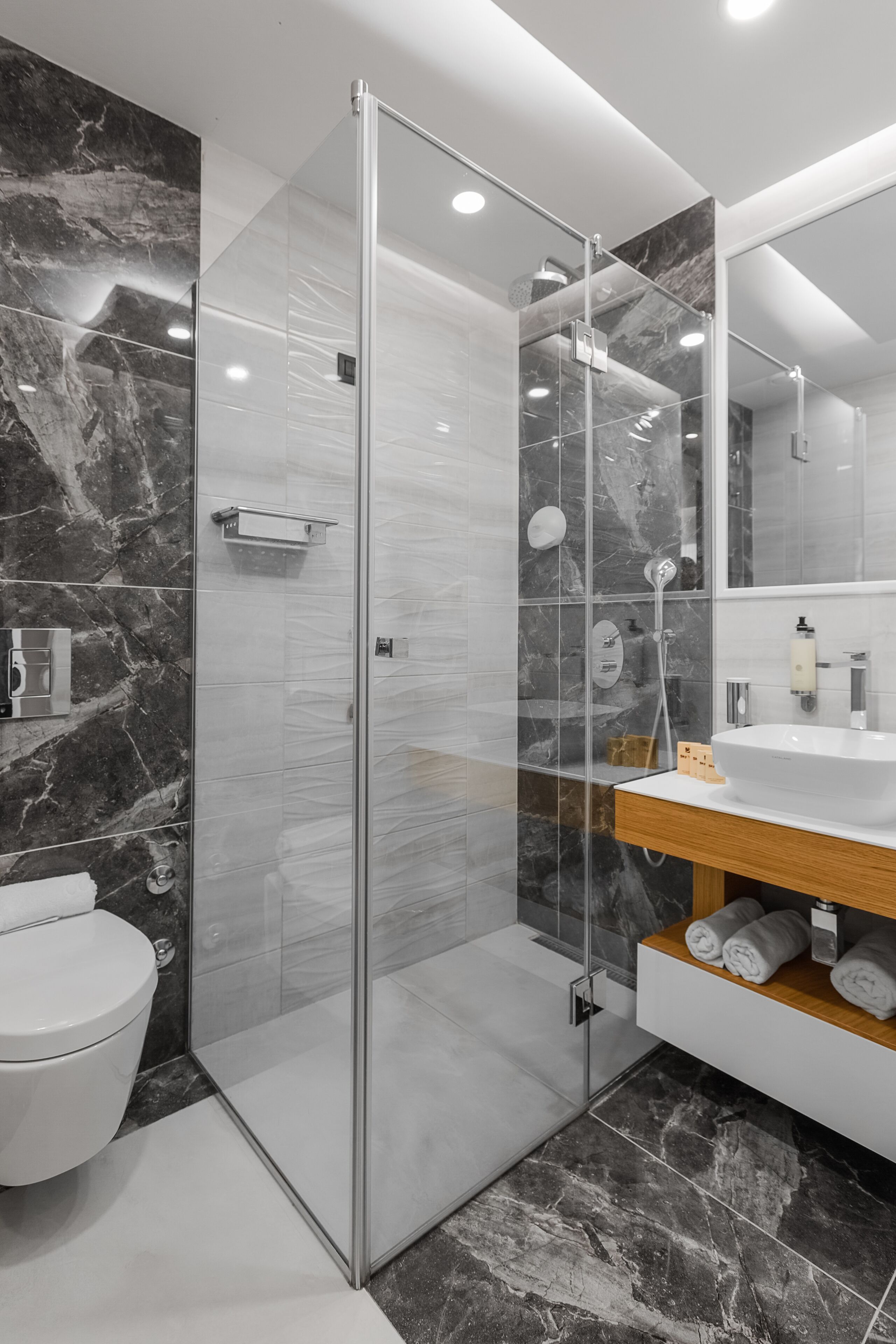 Une salle de bain moderne avec une douche à parois de verre, un lavabo blanc et des murs en marbre.
