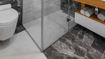 Une salle de bain moderne avec une douche à parois de verre, un lavabo blanc et des murs en marbre.
