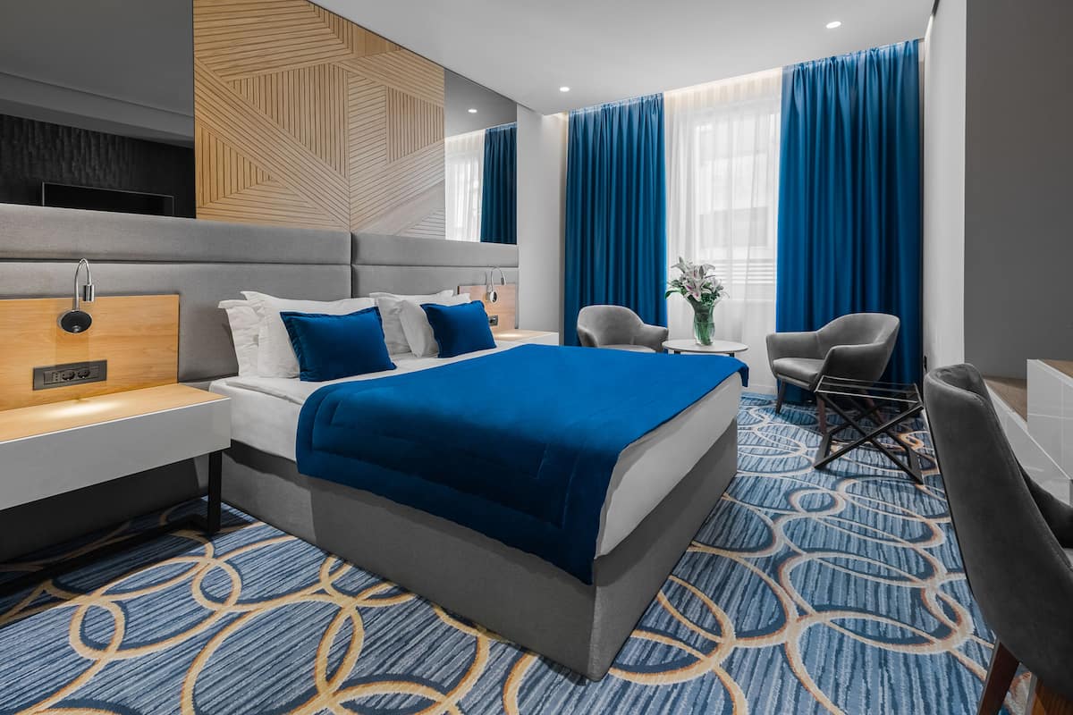 A modern hotel room with a large bed, a desk, a chair, and a small table with a vase of flowers.