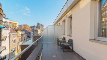 Un balcon avec vue sur la ville, une rambarde en verre et deux chaises.