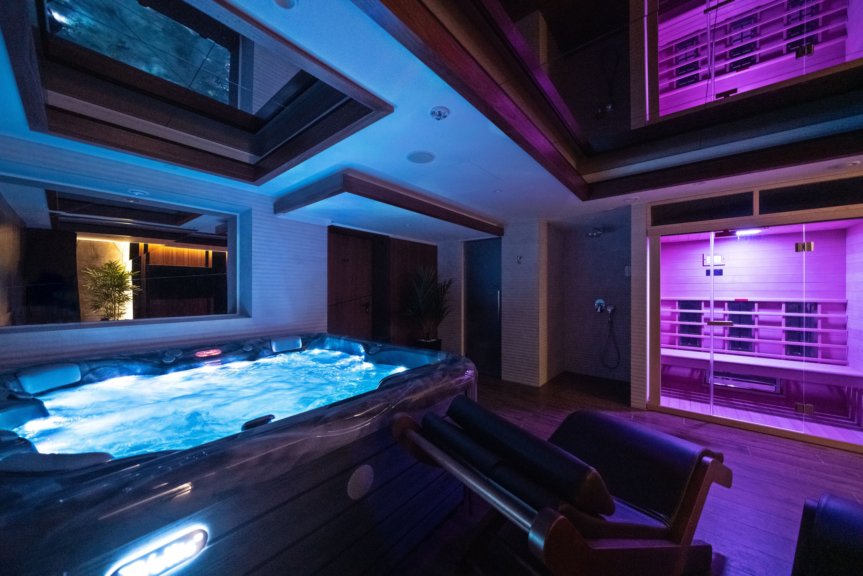 A modern spa area with a hot tub, wooden seating, and a glass-enclosed shower area.