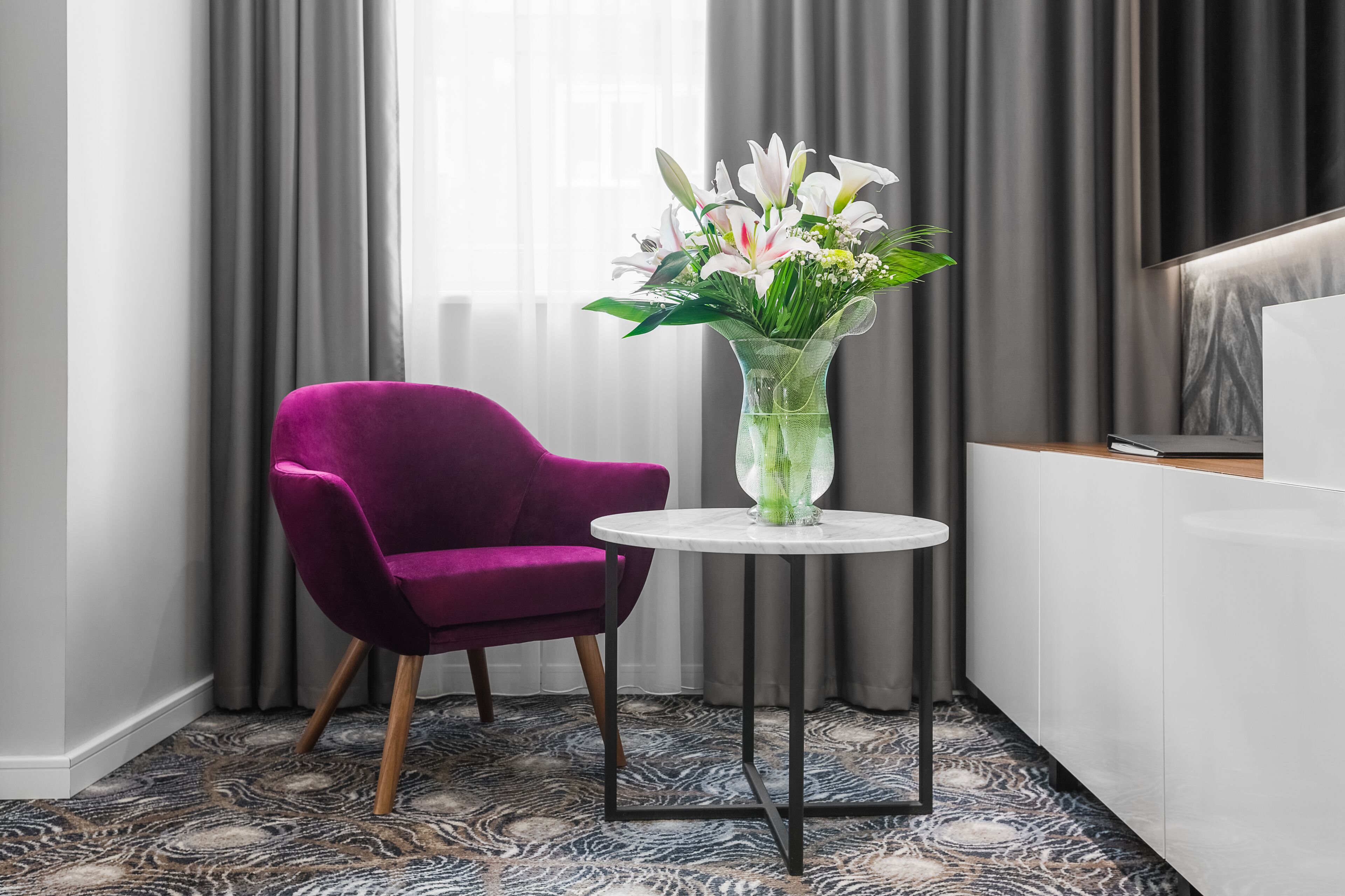 A modern room with a purple armchair, a round table with a vase of flowers, and a minimalist design.