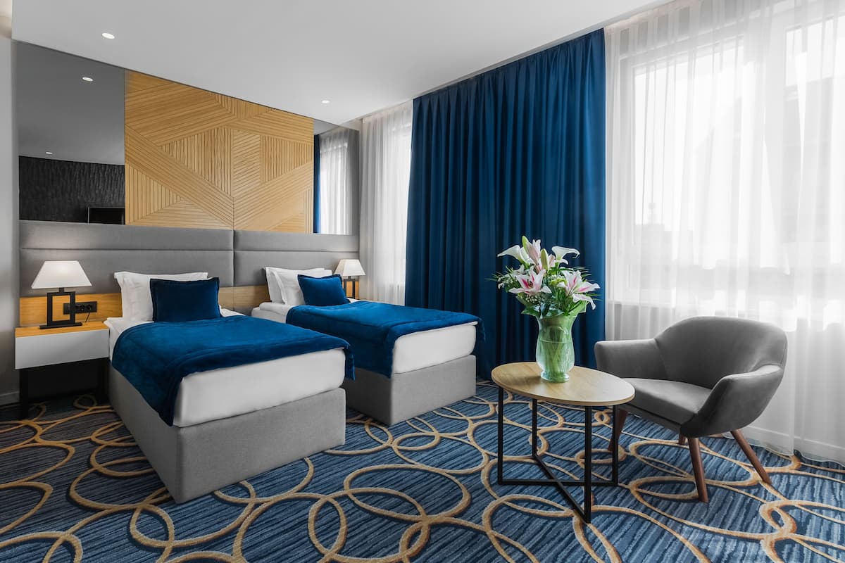A hotel room with two beds, a sitting area, a small table, and a chair.