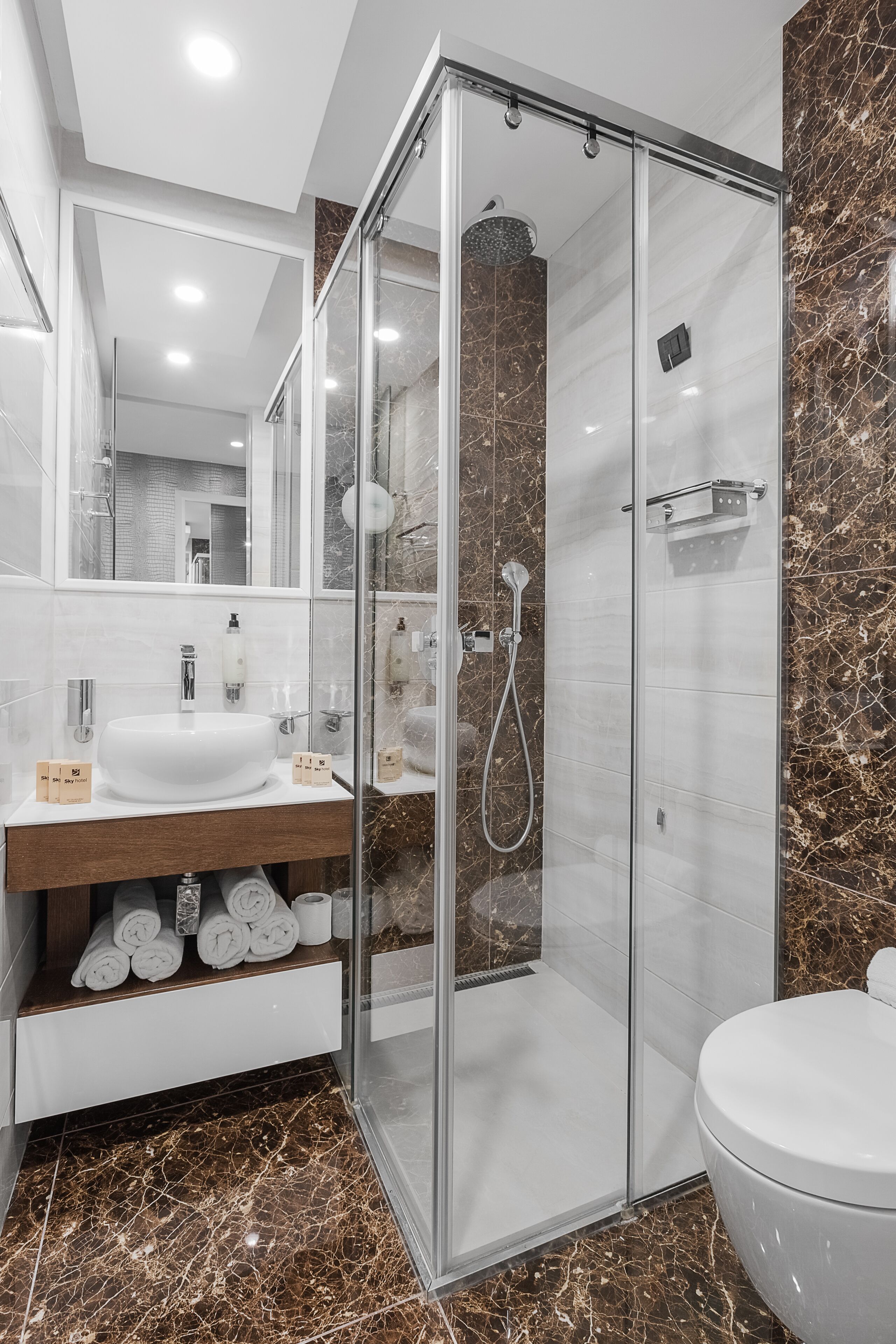 A modern bathroom with a glass-enclosed shower, a white sink, and marble flooring.