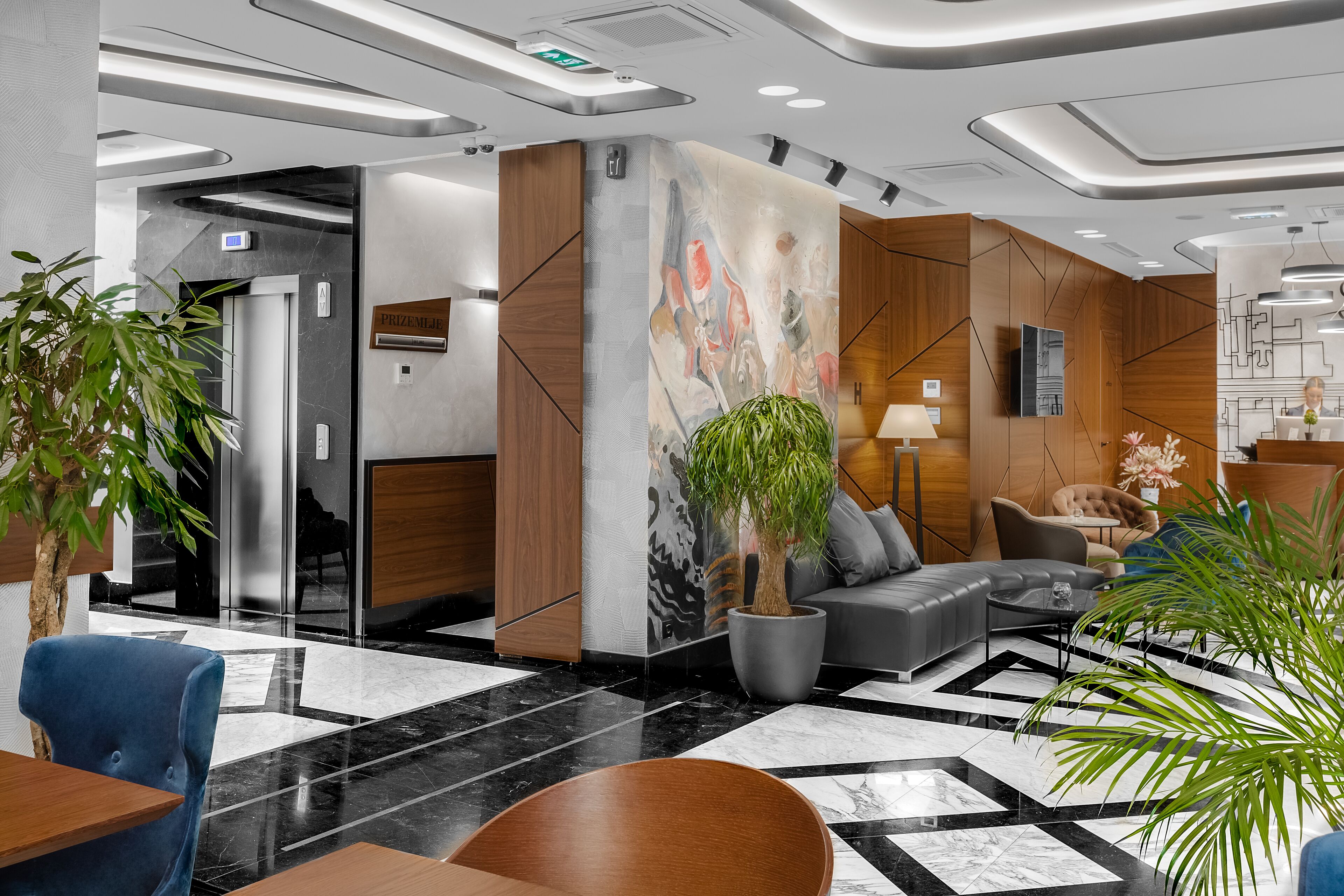 A modern lobby with a marble floor, a reception desk, a sofa, and a potted plant.
