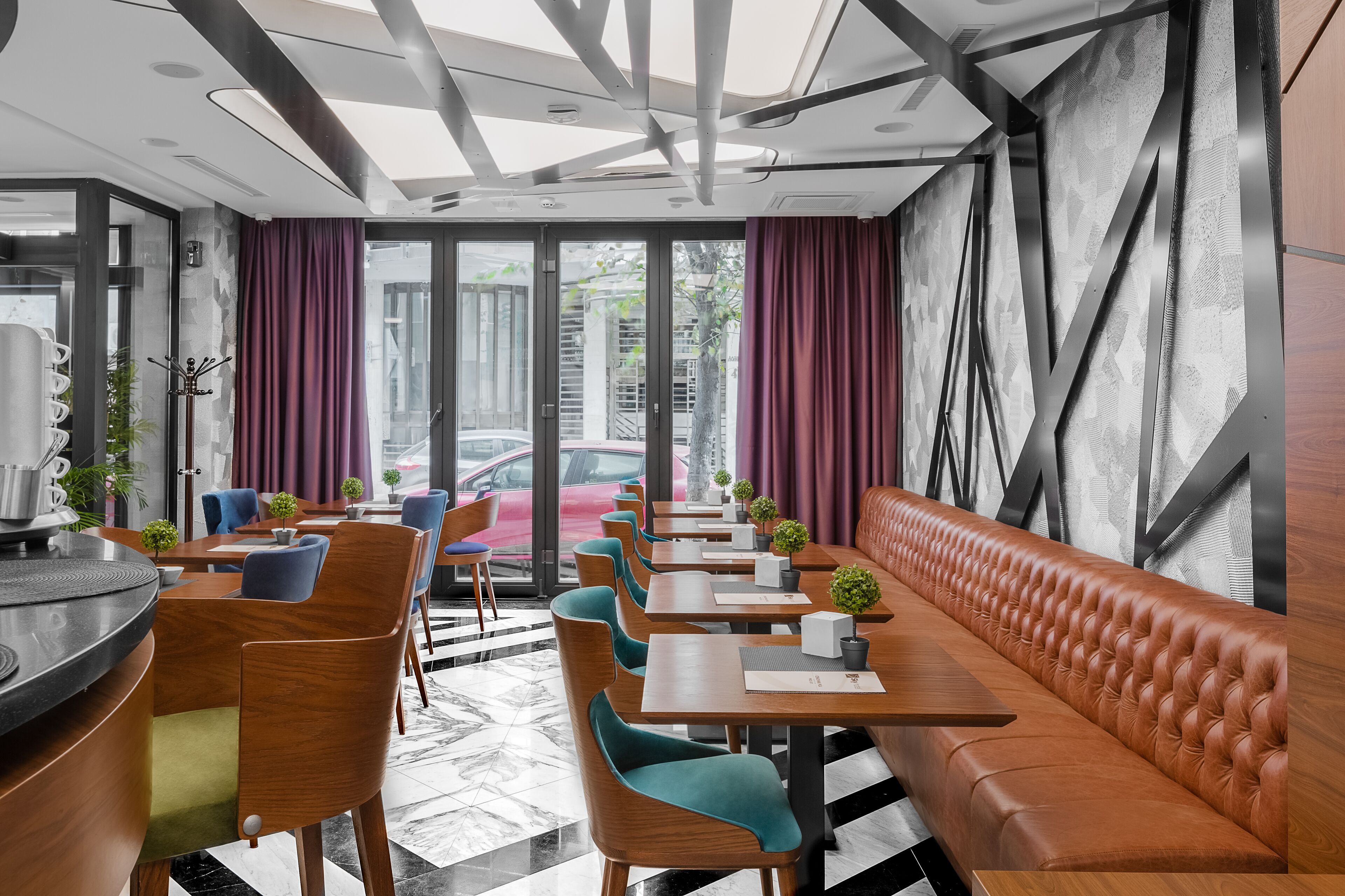Un restaurant moderne avec un long banc en bois, des chaises de couleur turquoise et un sol carrelé en noir et blanc.