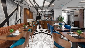 A modern restaurant with leather booths, wooden tables, and blue chairs. There is a bar area in the background. - Sky hotel (Belgrade)