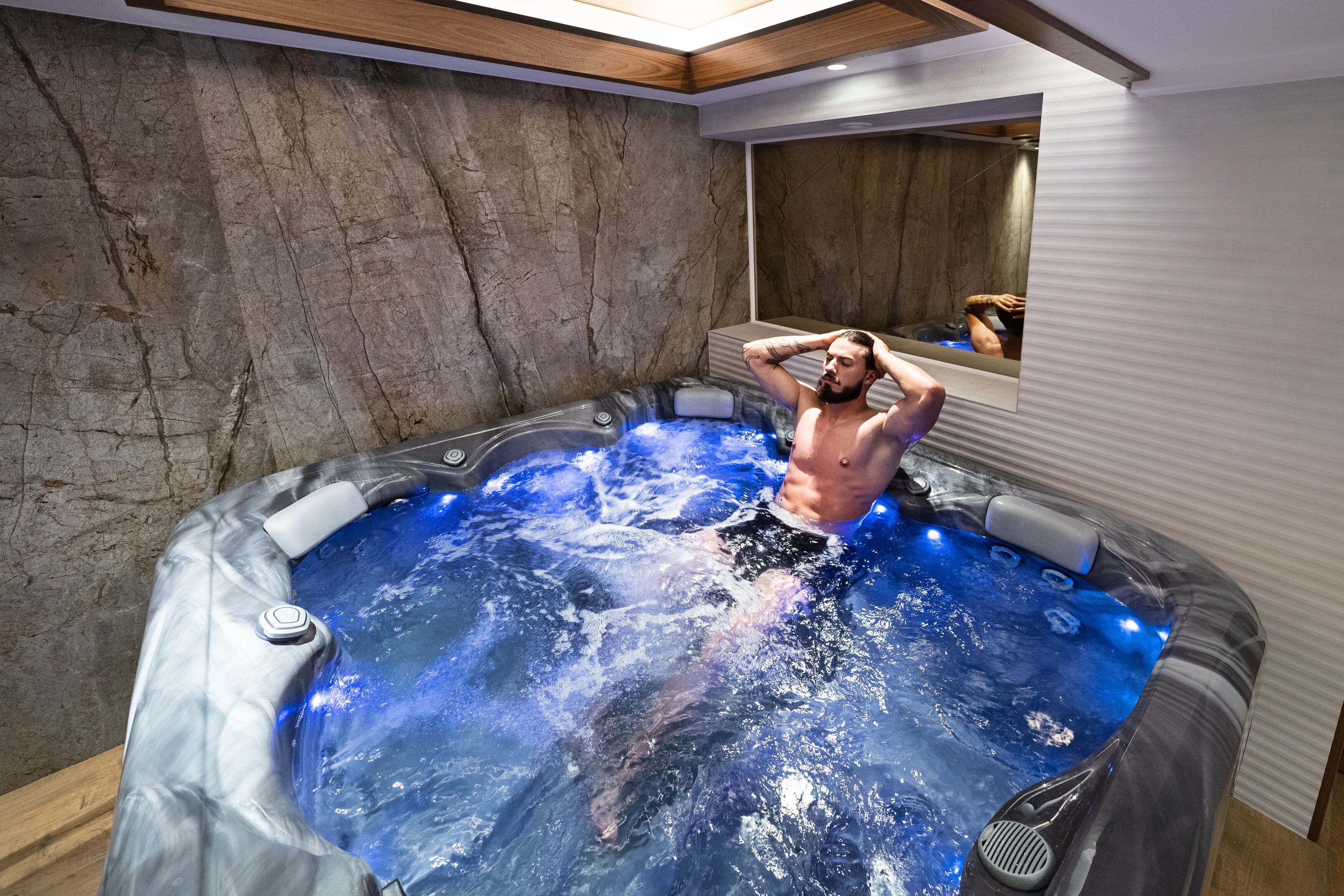 A man in a hot tub with a wooden ceiling and a stone wall.
