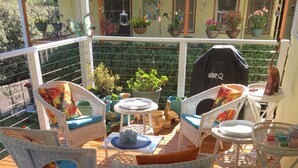 A wooden deck with white wicker furniture, including chairs and tables, and potted plants. - The Best Exotic Magnolia Cottage (Bundanoon)