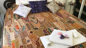A bed with a colorful quilt, multiple pillows, and a rolled towel with a lavender flower on a bedside table. - The Best Exotic Magnolia Cottage (Bundanoon)