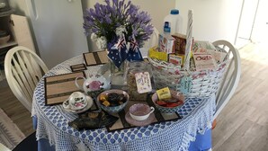 A dining table with a crocheted tablecloth, a vase with flowers, and various food items and condiments. - The Best Exotic Magnolia Cottage (Bundanoon)