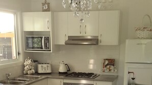 A kitchen with white cabinets, a microwave, an oven, a sink, and a dining table with a blue tablecloth. - The Best Exotic Magnolia Cottage (Bundanoon)