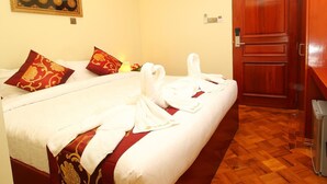 Habitación de hotel con cama, dos almohadas rojas, una toalla blanca, una puerta de madera y suelo de madera.