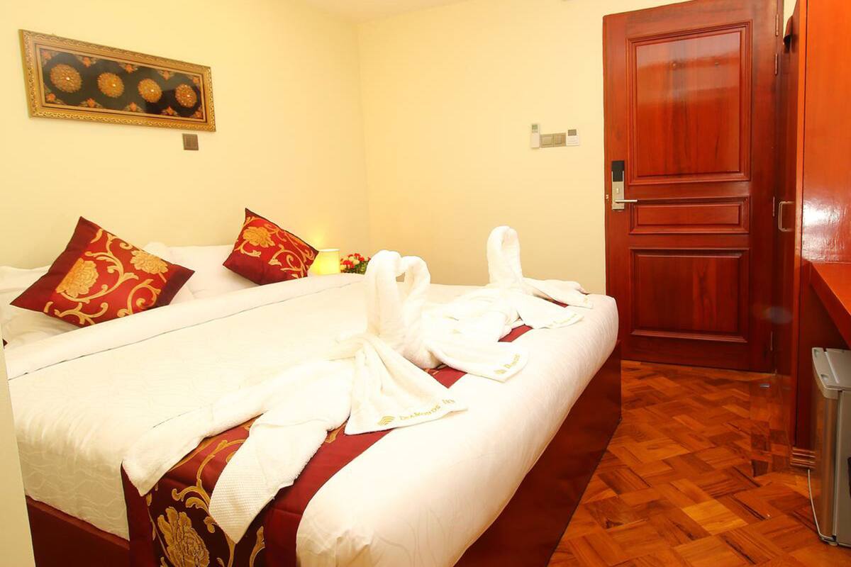Habitación de hotel con cama, dos almohadas rojas, una toalla blanca, una puerta de madera y suelo de madera.