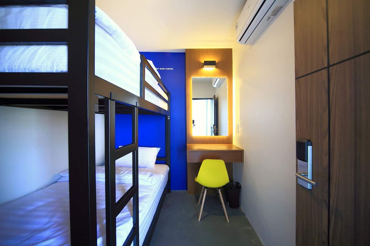A compact hotel room with bunk beds, a desk, a chair, and a mirror.