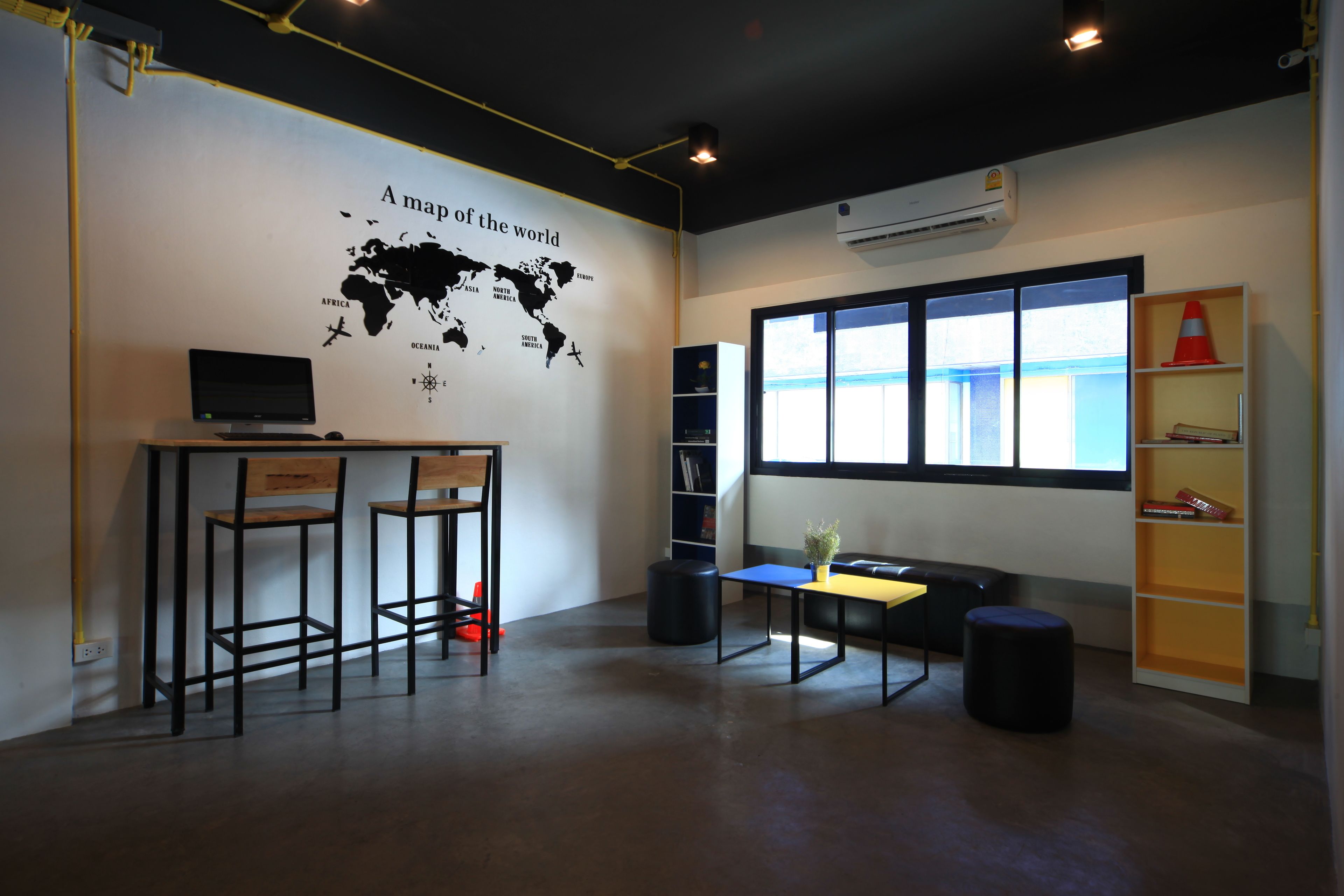 Un espacio de oficina moderno con un mapa del mundo en la pared, un escritorio con dos sillas, una estantería y una ventana con persianas.