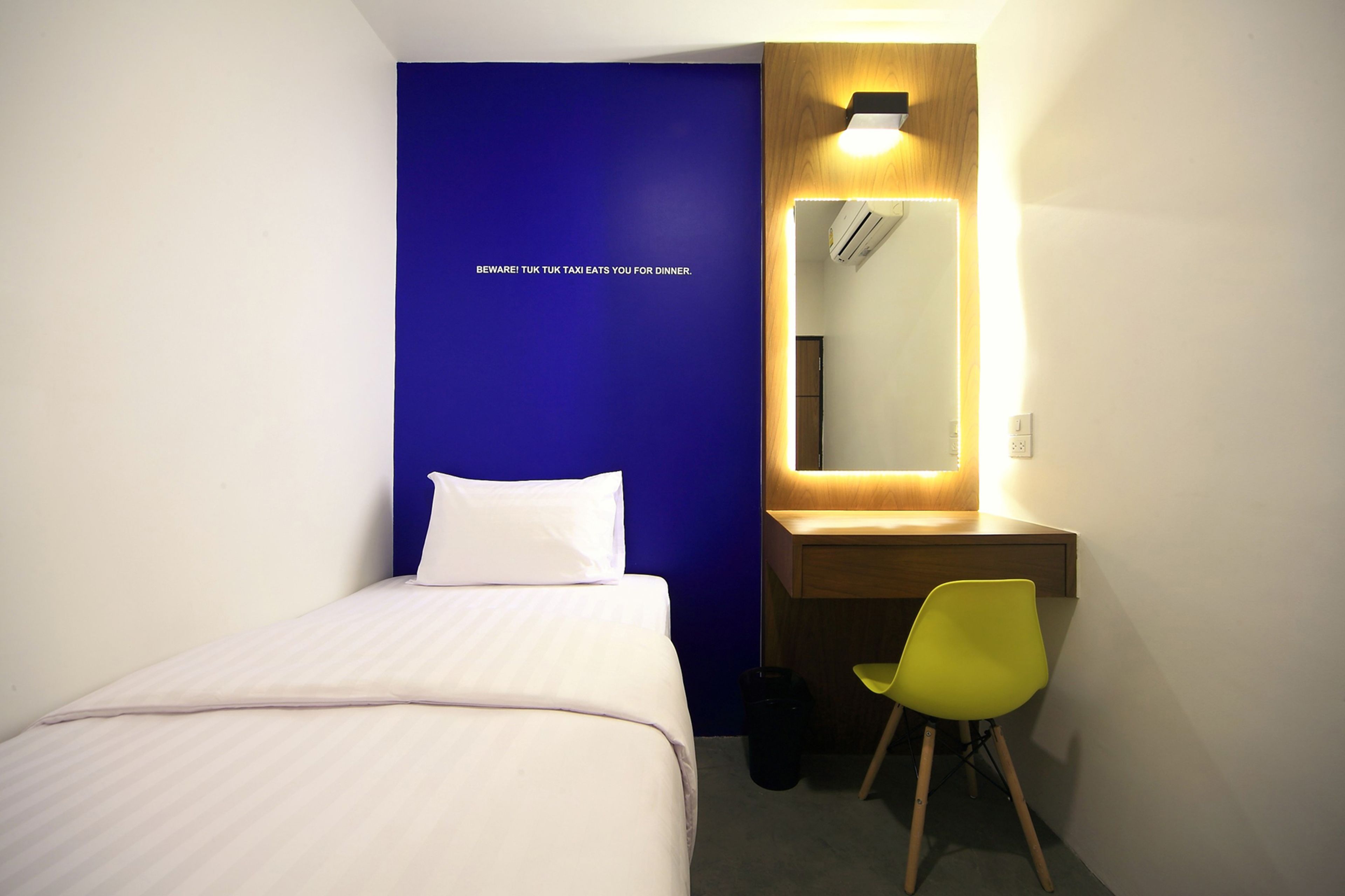 A hotel room with a bed, a desk, a mirror, and a yellow chair.