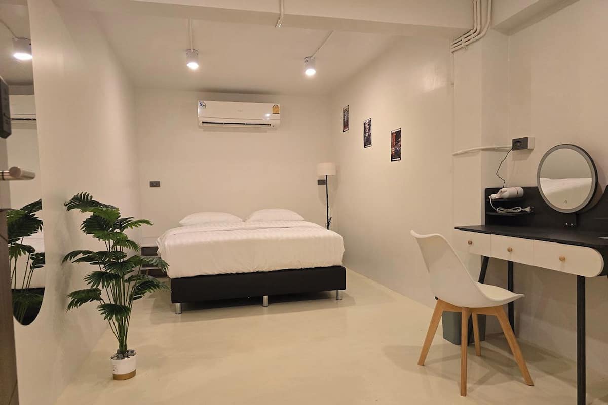 A modern bedroom with a bed, a desk, a chair, an air conditioner, and a potted plant.