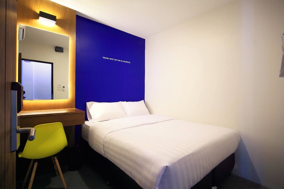 A hotel room with a bed, a desk, a chair, and a mirror.