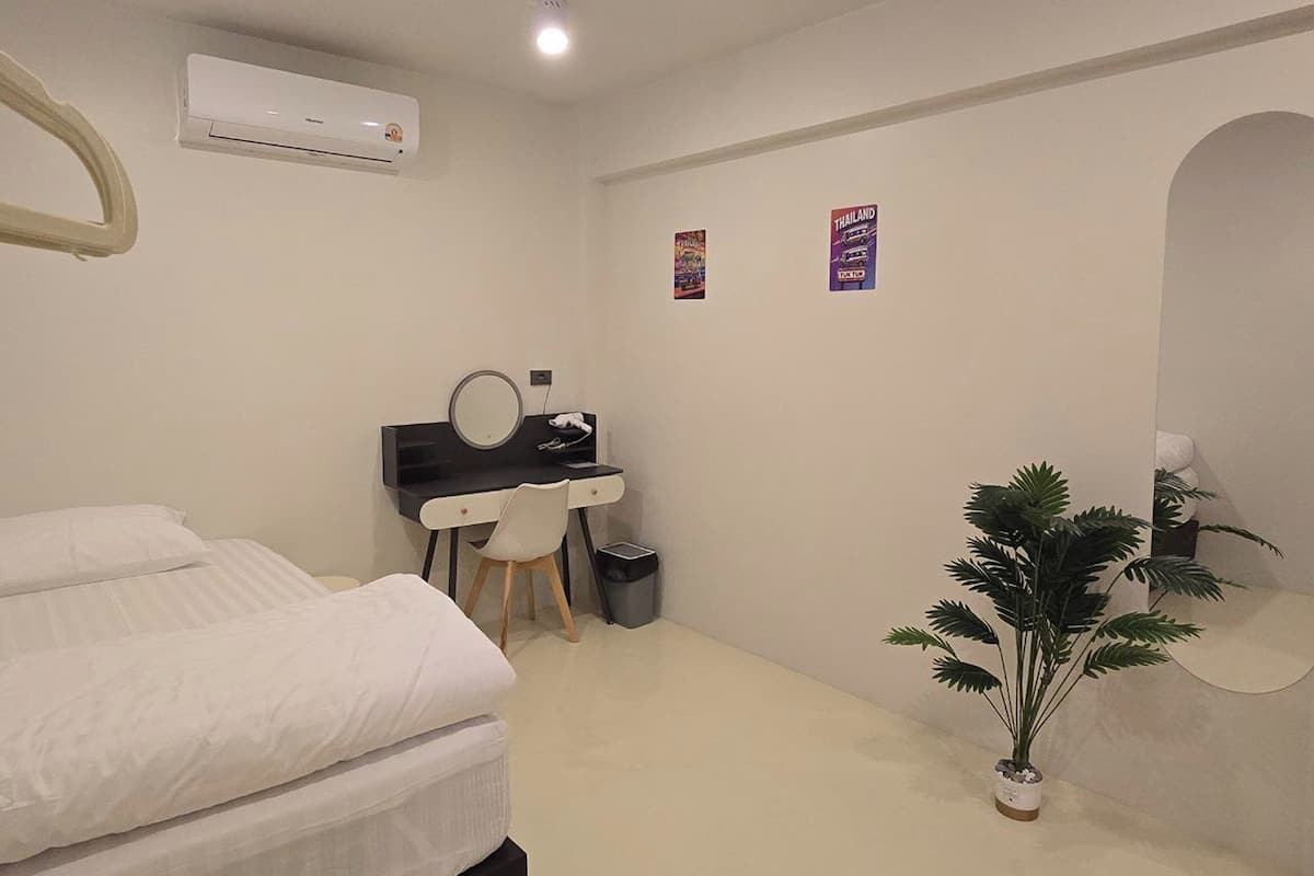 A bedroom with a bed, a desk with a chair, an air conditioner, and a potted plant.