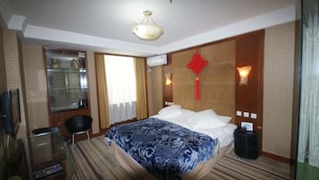 A hotel room with a bed, a desk with a chair, a television, and a window with blinds.
