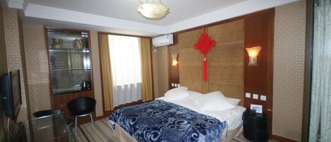 A hotel room with a bed, a desk with a chair, a television, and a window with blinds.