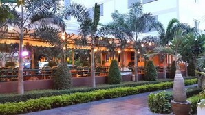 A courtyard with palm trees, a pathway, and a building with a warm-lit entrance. - Zaza Hotel (Samut Prakan)