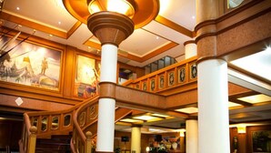 A grand lobby with a central staircase, ornate columns, and a high ceiling with decorative lighting. - Zaza Hotel (Samut Prakan)