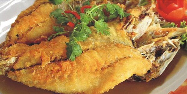 Un plato de pescado frito adornado con hierbas y chiles rojos.