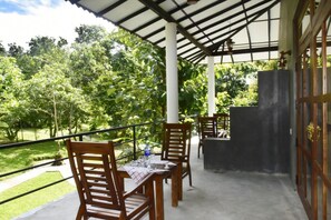 A covered outdoor dining area with wooden chairs and tables, a grill, and a view of a lush garden. - Safari Queens Resort (Udawalawa)