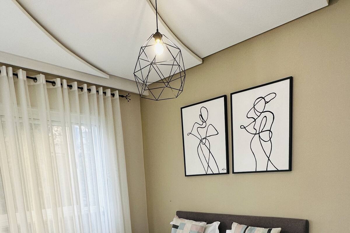 Une chambre à coucher comprenant un lit, une table de chevet, une commode, une lampe et deux œuvres d’art murales.