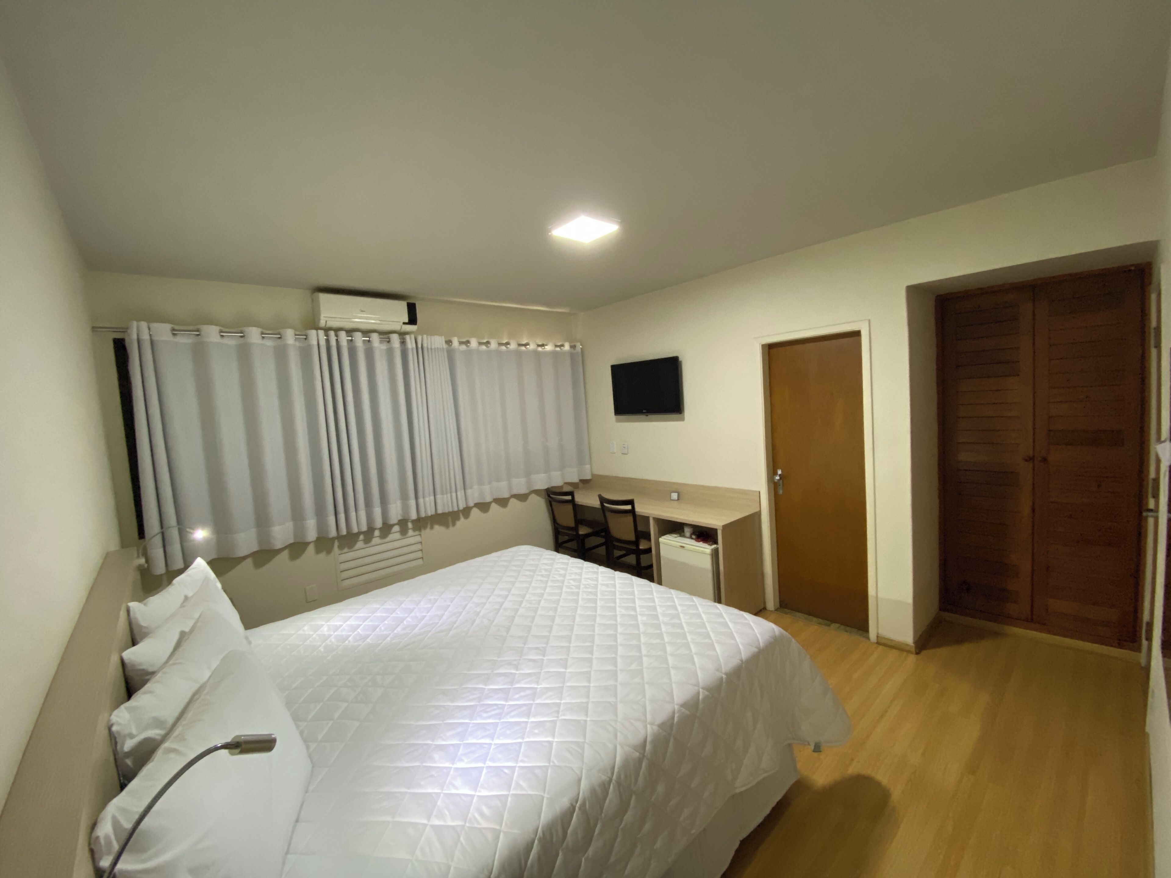 A bedroom with a bed, a desk, a television, and a wardrobe.