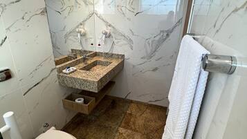 A bathroom with a marble wall, a granite sink, a toilet, and a towel rack.