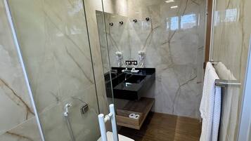 Um banheiro moderno com box de vidro, vaso sanitário, pia com bancada preta e toucador de madeira.