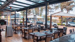 An outdoor cafe with wooden tables and chairs, umbrellas, and a grill. - HD Plaza Hotel (Assis)