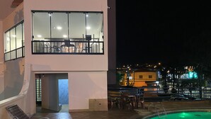 A hotel with a pool area, outdoor seating, and a view of the city at night. - HD Plaza Hotel (Assis)