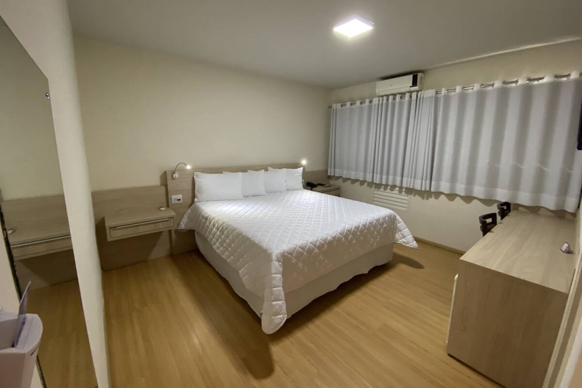 A neatly arranged bedroom with a bed, bedside tables, a desk, and a window with curtains.
