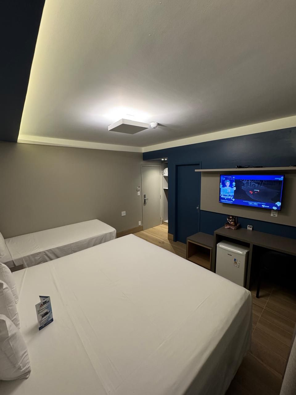 Habitación de hotel con dos camas individuales, un escritorio pequeño con televisión y una lámpara en el techo.