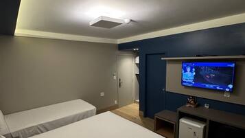Habitación de hotel con dos camas individuales, un escritorio pequeño con televisión y una lámpara en el techo.