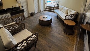 A modern interior with a sofa, wicker chairs, a round coffee table, and a view of a pool and outdoor area. - HD Plaza Hotel (Assis)