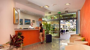 A hotel reception area with a counter, a receptionist, and a view of the outdoor seating area. - Hotel Antares (Alba Adriatica)