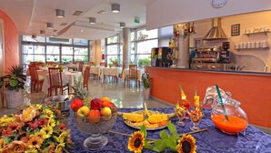 A hotel dining area with tables set for breakfast, a kitchen in the background, and a view of the outdoors. - Hotel Antares (Alba Adriatica)