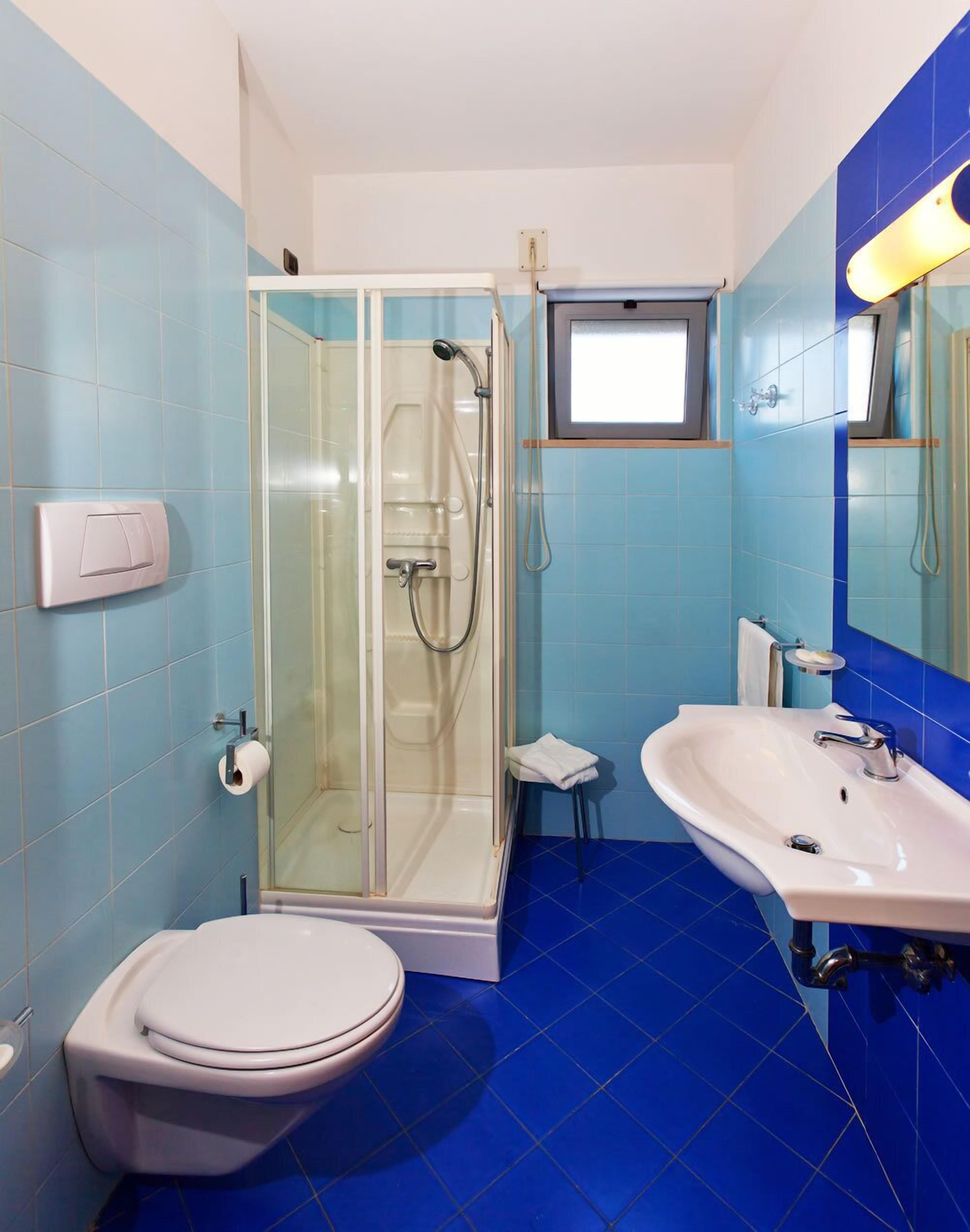 Un baño con ducha de vidrio, inodoro blanco y lavamanos con espejo.